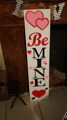 a wooden sign that says be mine with hearts hanging on the wall next to a fireplace