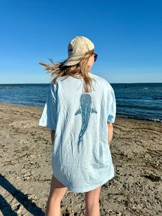 a woman standing on top of a sandy beach next to the ocean wearing a blue dolphin t - shirt