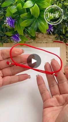 two hands are holding red string and one hand is holding a white piece of paper