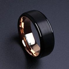 a black and gold wedding band with an inscription on the inside, in front of a dark background