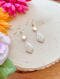 a pair of white earrings sitting on top of a wooden table next to pink flowers