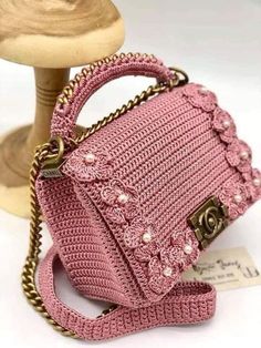 a pink crocheted purse sitting on top of a wooden table next to a mannequin head