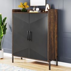 a black cabinet with a wooden top next to a potted plant and a mirror on the wall