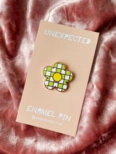 a pin with a flower on it sitting on a pink blanket next to a card