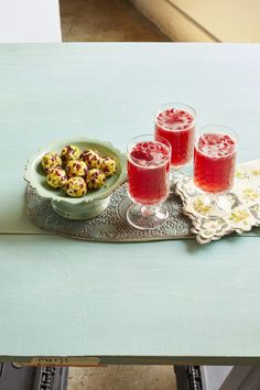 three glasses of red liquid sit on a tray next to two bowls of cookies and a bowl of fruit