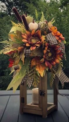 a wooden lantern filled with lots of flowers and leaves on top of a table next to a candle