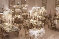 a room filled with lots of tables covered in white flowers and candles next to tall vases