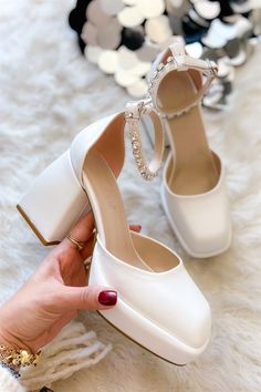 a woman's hand is holding a pair of white high heels