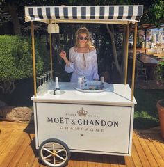 a woman is standing behind a cart selling champagne and ice cream on the deck of a house