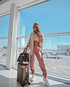 a woman standing next to an airport window with her suitcase and handbag in front of her