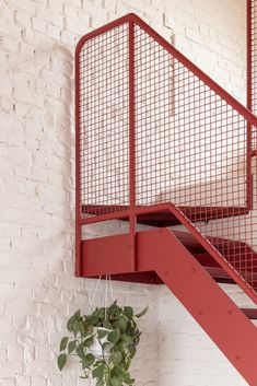 a red metal staircase next to a white brick wall with a potted plant on it