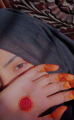 a woman with her hands on her face covered by a black head scarf and orange nail polish