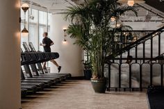 a woman is running on a treadmill in a hotel lobby with palm trees and potted plants