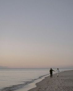 a man and woman holding hands while walking on the beach at sunset with kites flying in the air