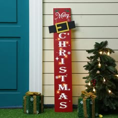 a merry christmas sign next to two presents on the grass near a blue front door