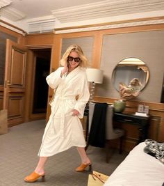 a woman in a bathrobe walking through a hotel room