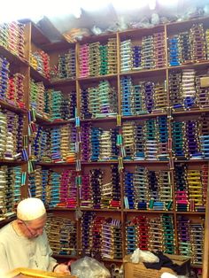 a man sitting at a table in front of a wall full of colorful glasses and other items