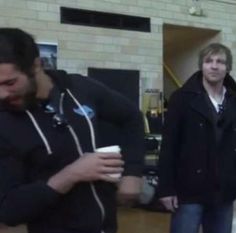 two men standing next to each other holding coffee cups