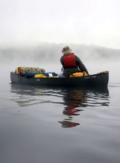 a man in a canoe paddling through the water on a foggy, overcast day