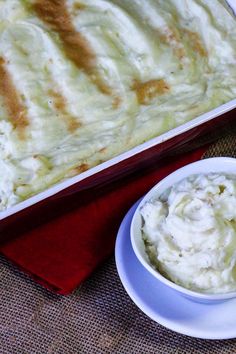 a casserole dish with mashed potatoes on a red cloth next to a white bowl