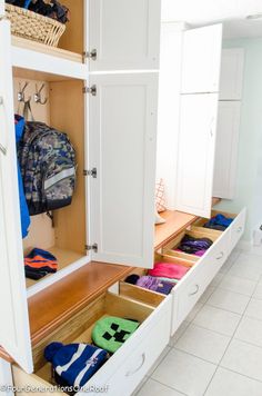 an open cabinet in the middle of a kitchen filled with clothes and backpacks on it