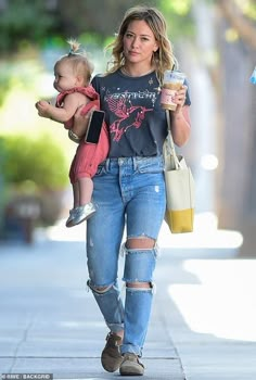 a woman walking down the street with a baby in her arms and holding a cup