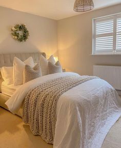 a white bed sitting next to a window in a bedroom under a light fixture and a wreath on the wall