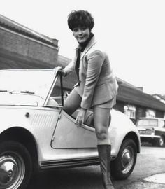 an old photo of a woman leaning on the hood of a car in front of a building