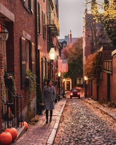 a person walking down a cobblestone street in an alleyway with pumpkins on the ground