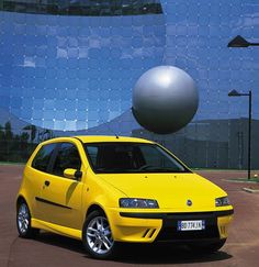 a yellow car parked in front of a building with a large metal ball on it's roof