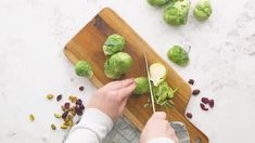 a person cutting brussels sprouts on a wooden cutting board with other vegetables nearby