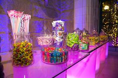 there are many candy in glass jars on the counter with purple lights behind them,