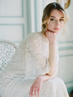 a woman in a white dress sitting on a chair with her hand under her chin