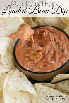 a tortilla chip being dipped with salsa in a black bowl surrounded by tortillas