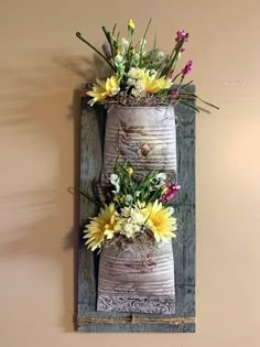 two vases with yellow and white flowers are hanging on a wall