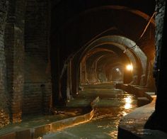 a dark tunnel with water running through it and lights on at the end in the distance