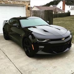 a black chevrolet camaro parked in front of a house