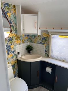 a bathroom with a toilet, sink and cabinets in it's own room that is decorated with tropical wallpaper