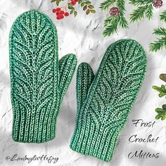 two green knitted mittens sitting on top of a white sheet with holly branches