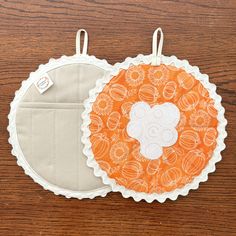 two orange and white pot holders sitting on top of a wooden table