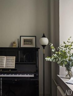 a black piano sitting in front of a window next to a lamp