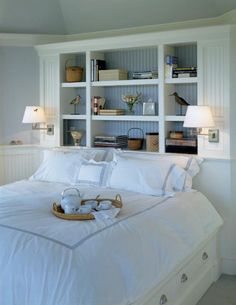 a bed with white linens and pillows in a bedroom next to a book shelf