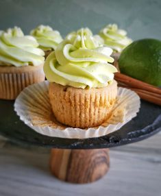 cupcakes with green frosting and lime on a black plate next to some cinnamon sticks