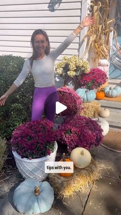 a woman standing on top of a pile of fake pumpkins next to purple flowers