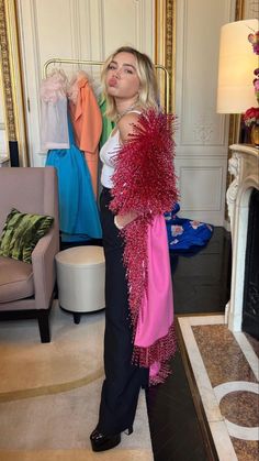 a woman standing in front of a mirror holding a pink scarf over her shoulder and looking at the camera