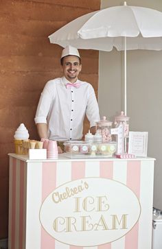 a man standing behind an ice cream stand with pink and white stripes on the counter