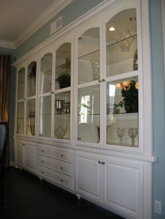 a white china cabinet with glass doors and drawers in the middle of a dining room