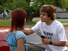 a young man is talking to a woman in front of a car