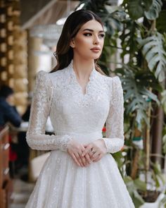 a woman wearing a white wedding dress with long sleeves and a high neckline is posing for the camera