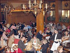 a large group of people sitting at tables in a dining room with chandeliers